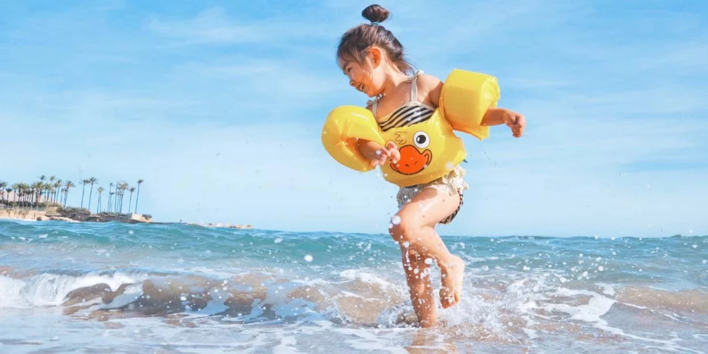 young child in water wings playing at the ocean