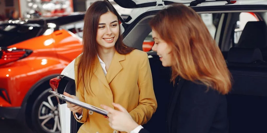 two smiling women looking at paperwork in car dealership showroom